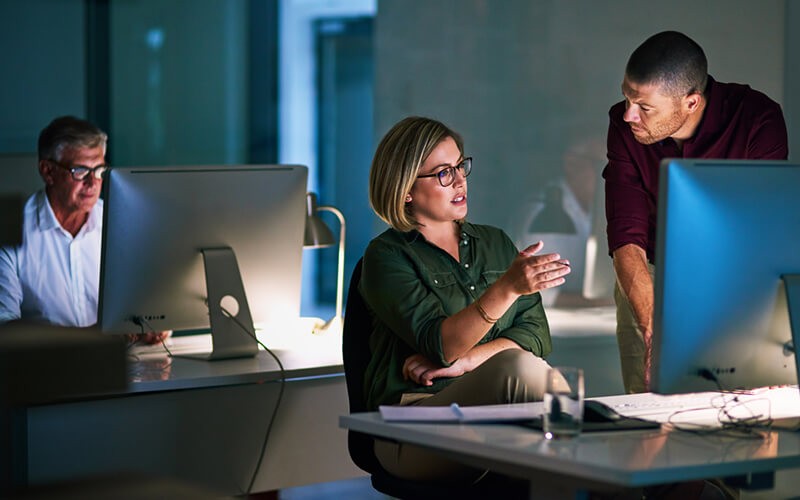 Colleagues analyzing data on computer in office at night