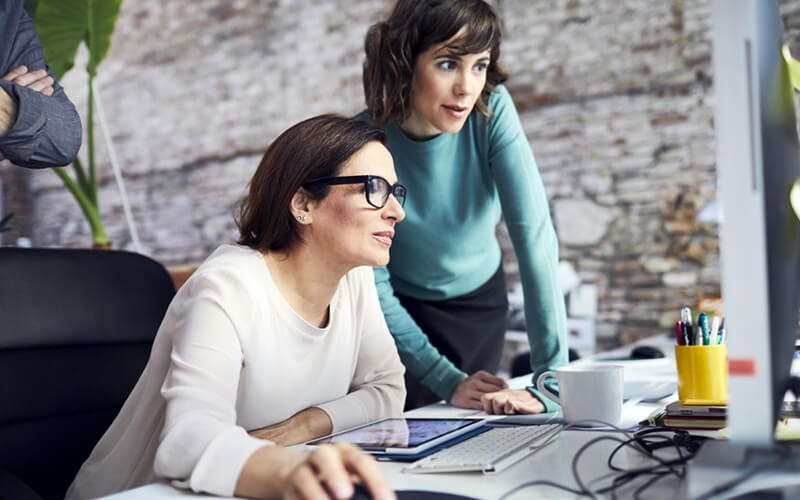 Two businesswomen looking at reports on desktop computer
