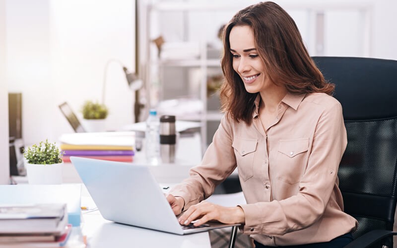 Smiling businesswoman works on laptop computer at desk